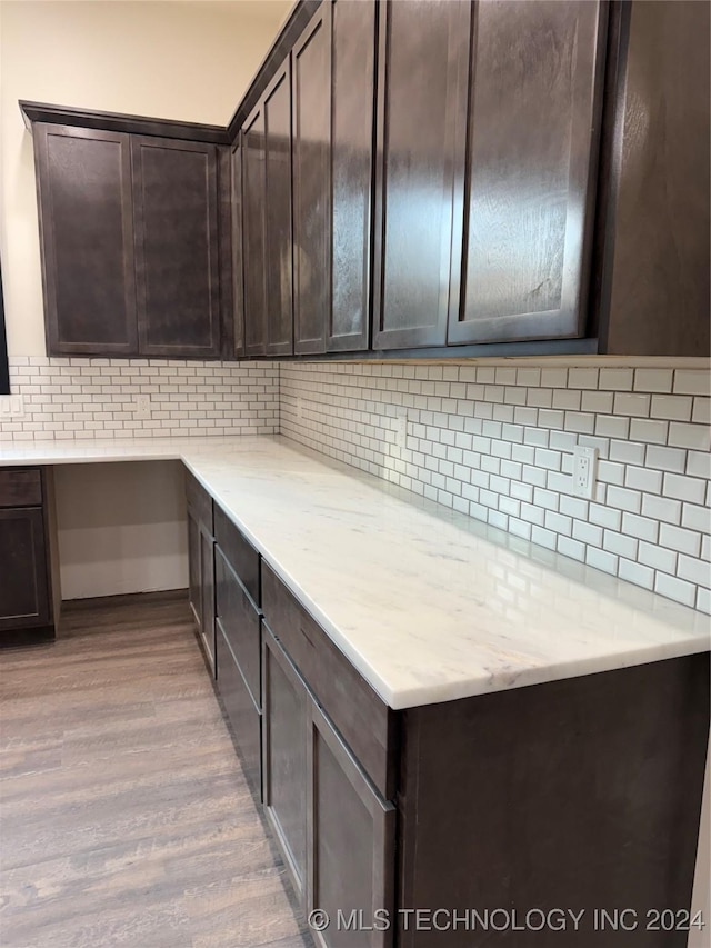 kitchen featuring light wood-type flooring, dark brown cabinetry, tasteful backsplash, and light stone counters