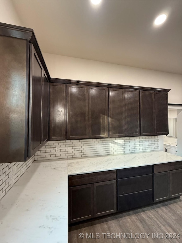 kitchen with dark hardwood / wood-style floors, light stone counters, dark brown cabinets, and backsplash