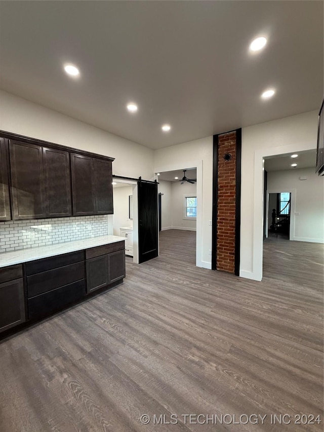 kitchen with hardwood / wood-style floors, a barn door, tasteful backsplash, and dark brown cabinetry