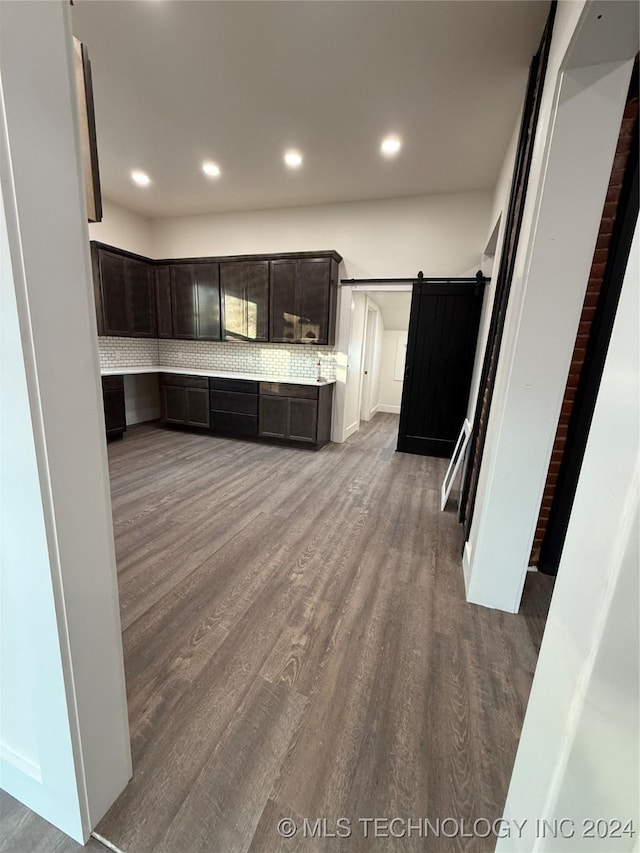 kitchen with hardwood / wood-style floors, a barn door, dark brown cabinetry, and tasteful backsplash