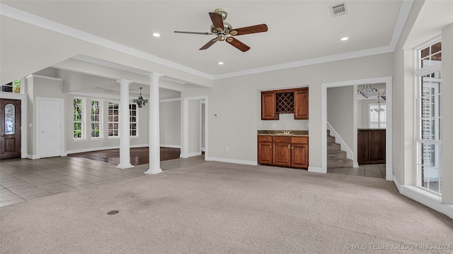 unfurnished living room featuring ceiling fan, ornamental molding, indoor wet bar, light colored carpet, and decorative columns