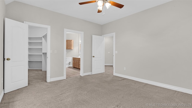 unfurnished bedroom with connected bathroom, a spacious closet, ceiling fan, and light carpet