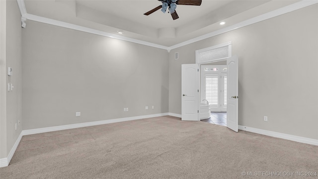 unfurnished room featuring a raised ceiling, ceiling fan, light colored carpet, and crown molding