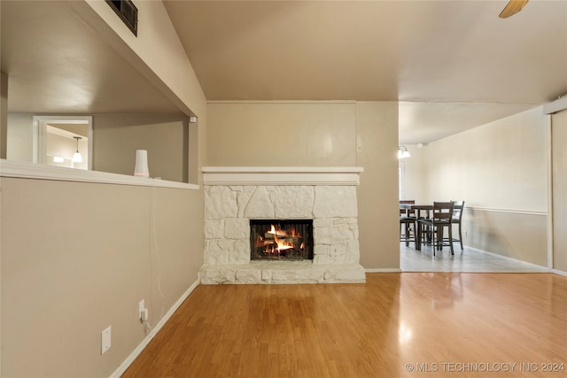 unfurnished living room with hardwood / wood-style flooring, ceiling fan, and a stone fireplace