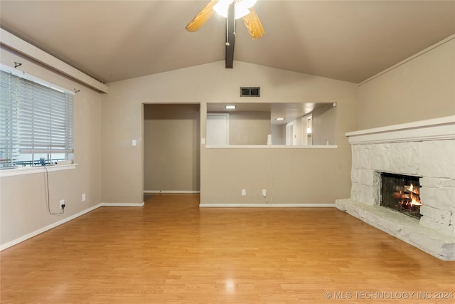 unfurnished living room featuring hardwood / wood-style floors, vaulted ceiling with beams, ceiling fan, and a stone fireplace