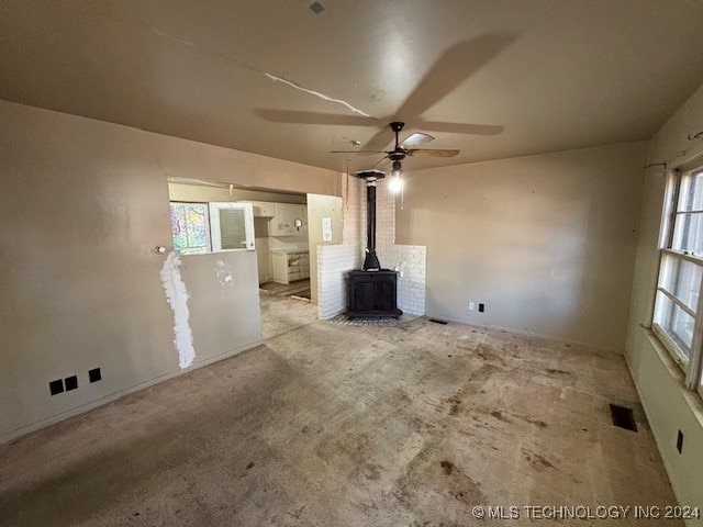 unfurnished living room featuring light carpet, a wood stove, and ceiling fan