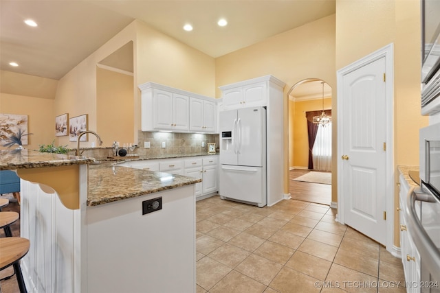 kitchen with kitchen peninsula, sink, dark stone countertops, white cabinets, and white fridge with ice dispenser