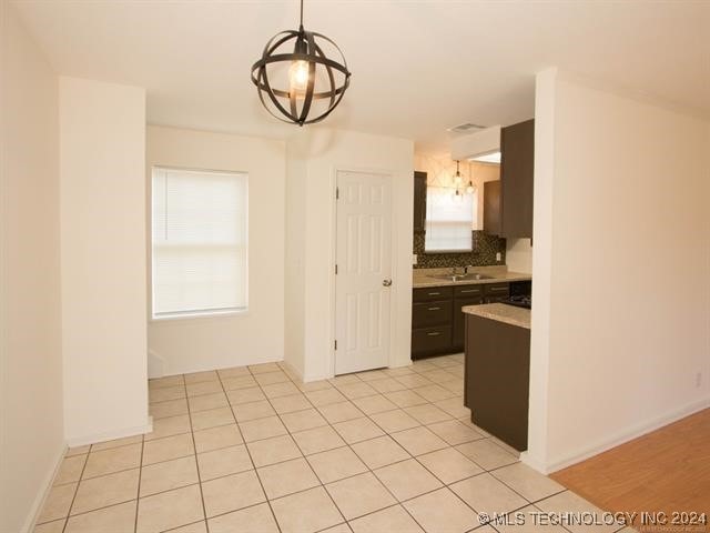 kitchen featuring pendant lighting, sink, decorative backsplash, light tile patterned floors, and dark brown cabinets