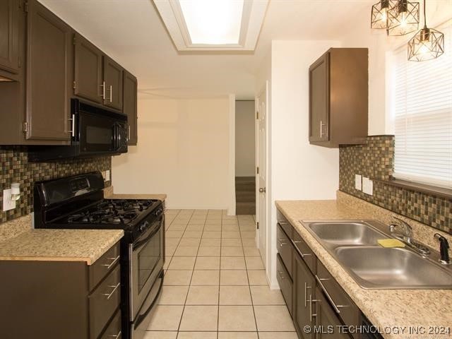 kitchen with tasteful backsplash, dark brown cabinetry, sink, black appliances, and light tile patterned floors