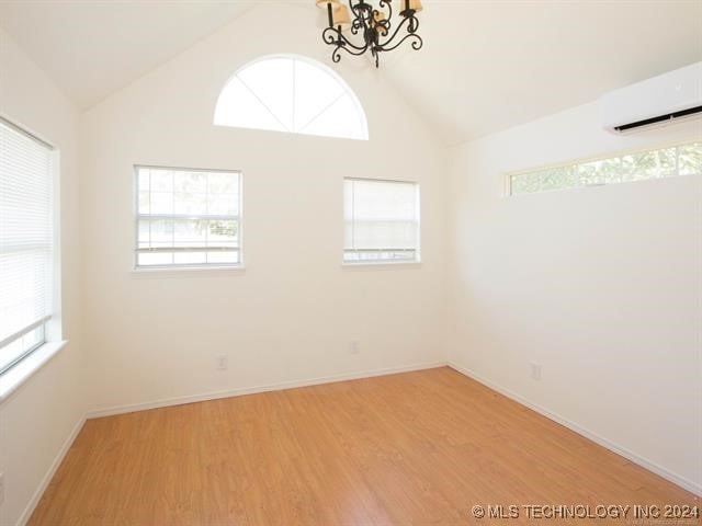 spare room with a wall unit AC, light hardwood / wood-style flooring, a chandelier, and lofted ceiling