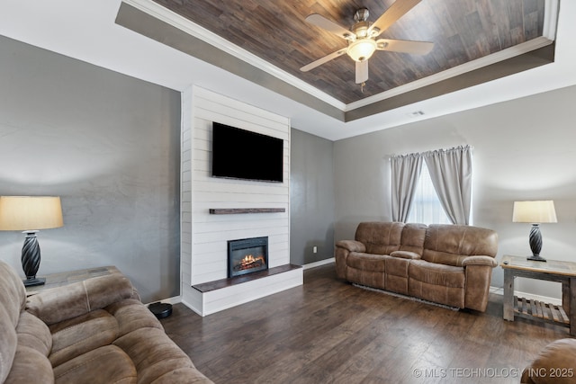 living room featuring wood ceiling, dark wood-type flooring, a tray ceiling, a fireplace, and ornamental molding