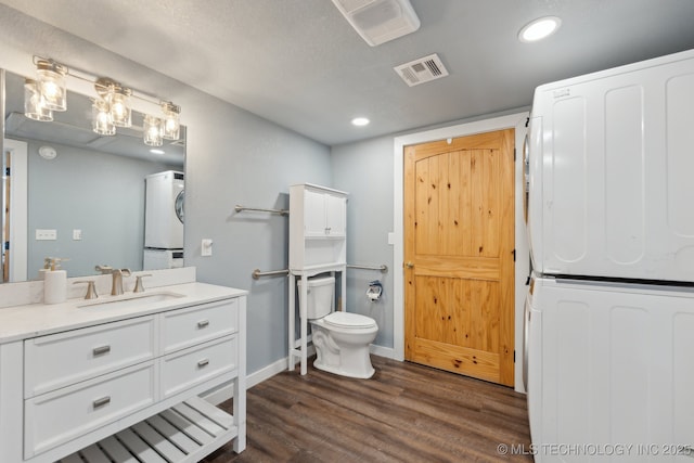 bathroom with stacked washing maching and dryer, hardwood / wood-style floors, vanity, and toilet