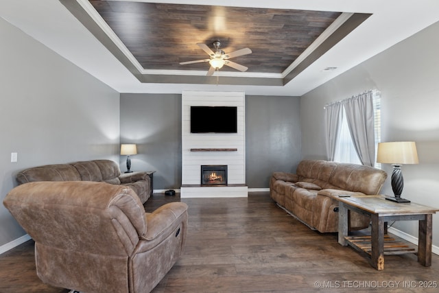 living room with a raised ceiling, ceiling fan, a fireplace, and dark hardwood / wood-style flooring