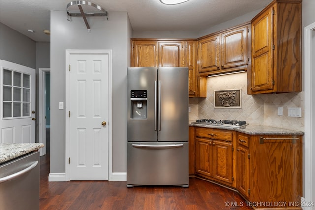 kitchen with backsplash, light stone countertops, a textured ceiling, appliances with stainless steel finishes, and dark hardwood / wood-style flooring