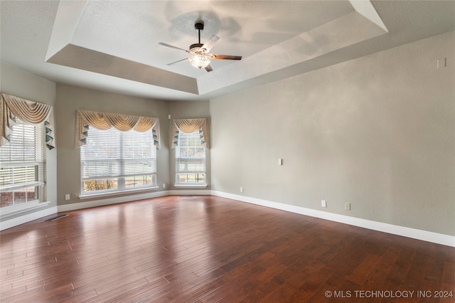 empty room with a raised ceiling, ceiling fan, and wood-type flooring