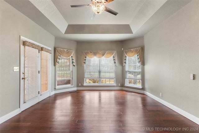 unfurnished dining area featuring a tray ceiling, ceiling fan, and dark wood-type flooring