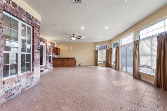 unfurnished living room featuring a wealth of natural light, light tile patterned floors, and ceiling fan