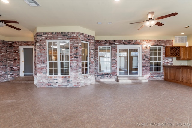 unfurnished living room featuring ceiling fan and brick wall