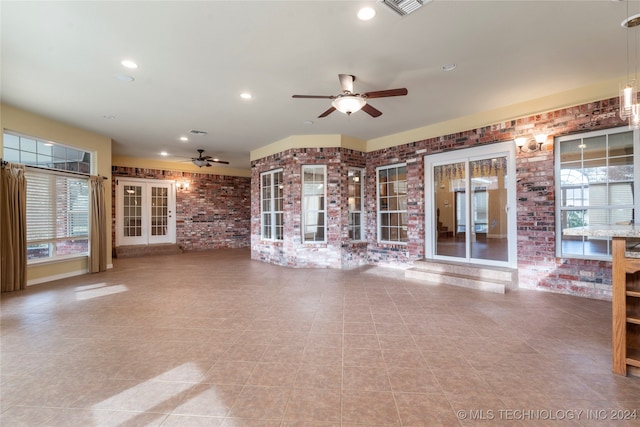 unfurnished living room featuring tile patterned floors, ceiling fan, and brick wall