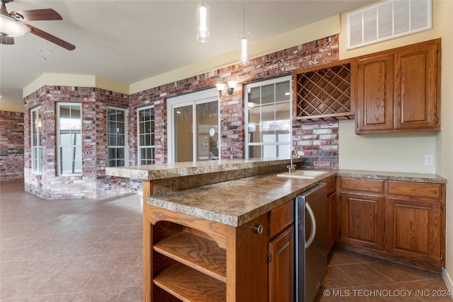 kitchen with ceiling fan, sink, hanging light fixtures, tile patterned flooring, and brick wall