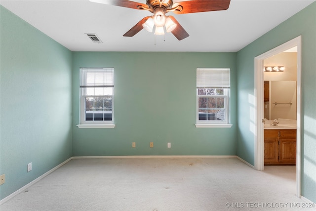 unfurnished bedroom with multiple windows, light carpet, and ensuite bath