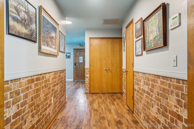 corridor with hardwood / wood-style floors and brick wall