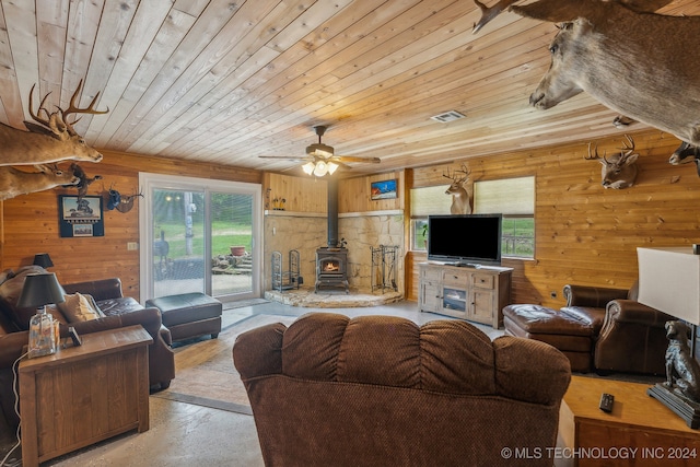 living room with a wood stove, ceiling fan, wooden walls, and wooden ceiling