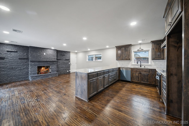 kitchen featuring pendant lighting, a large fireplace, stainless steel dishwasher, dark brown cabinetry, and kitchen peninsula