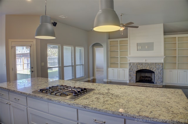 kitchen featuring hanging light fixtures, light stone countertops, a fireplace, white cabinetry, and stainless steel gas cooktop