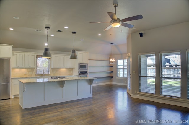 kitchen with white cabinets, light stone countertops, appliances with stainless steel finishes, a kitchen island, and dark hardwood / wood-style flooring