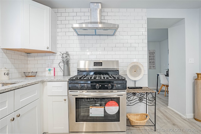 kitchen with wall chimney range hood, light stone counters, light hardwood / wood-style floors, white cabinets, and stainless steel range with gas stovetop