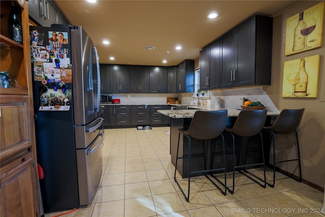 kitchen with appliances with stainless steel finishes, a kitchen breakfast bar, light stone counters, sink, and light tile patterned floors