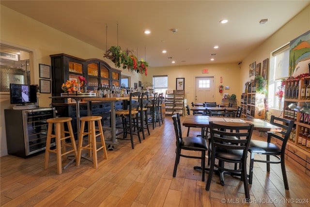 dining room featuring beverage cooler, indoor bar, and light wood-type flooring