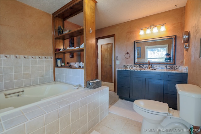 bathroom featuring vanity, a textured ceiling, a relaxing tiled tub, tile patterned flooring, and toilet