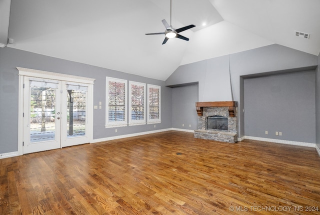 unfurnished living room featuring ceiling fan, french doors, a stone fireplace, hardwood / wood-style floors, and vaulted ceiling