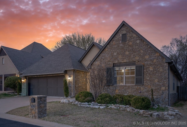 view of front of home featuring an attached garage, stone siding, driveway, and roof with shingles