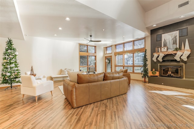 living room featuring a high ceiling, light wood-type flooring, a large fireplace, and ceiling fan