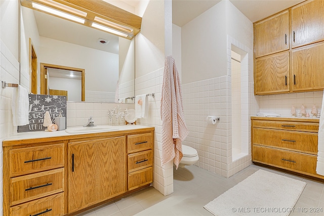 bathroom with tasteful backsplash, tile patterned flooring, toilet, vanity, and tile walls