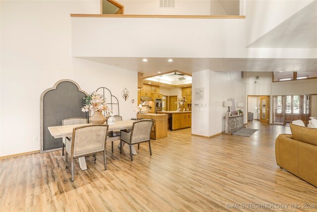 dining room with light wood-type flooring and a towering ceiling