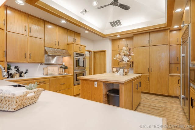 kitchen with white stovetop, a raised ceiling, light hardwood / wood-style flooring, a kitchen island, and stainless steel double oven