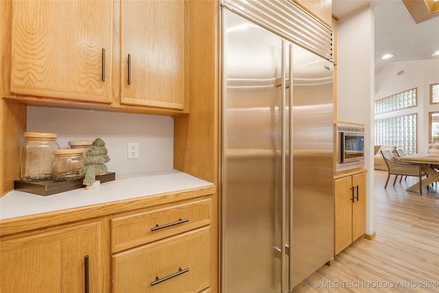 kitchen featuring light wood-type flooring, light brown cabinets, built in appliances, and vaulted ceiling