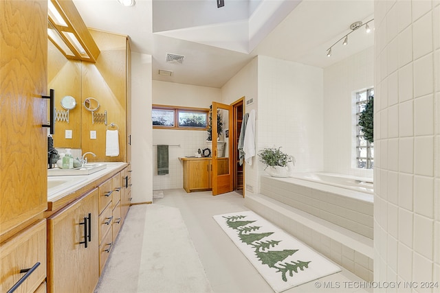 bathroom featuring tile patterned flooring, vanity, a healthy amount of sunlight, and a relaxing tiled tub