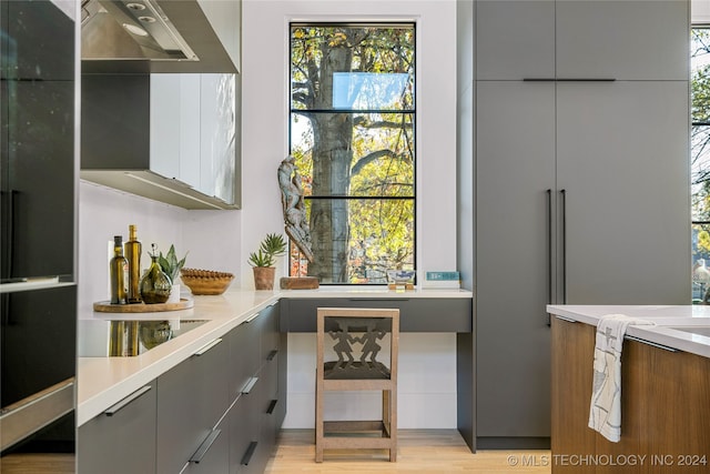 kitchen featuring black electric stovetop, wall chimney range hood, a wealth of natural light, and light hardwood / wood-style flooring