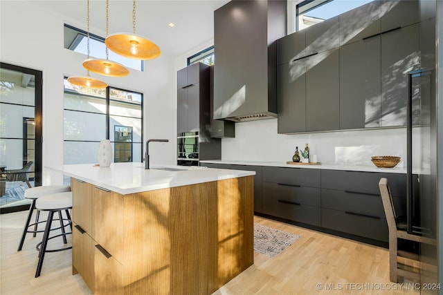 kitchen featuring a kitchen bar, sink, decorative light fixtures, light hardwood / wood-style floors, and an island with sink