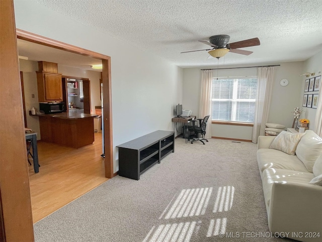 living room featuring ceiling fan, light hardwood / wood-style floors, and a textured ceiling