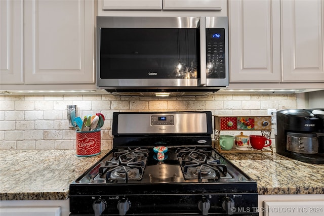 kitchen with backsplash, stone counters, white cabinetry, and black gas range oven