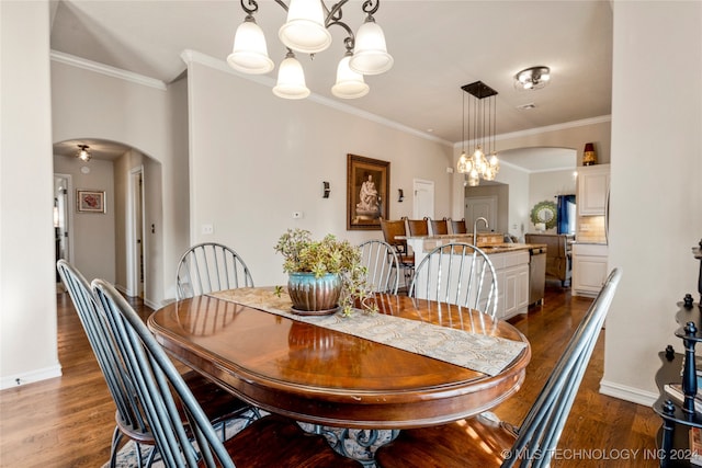 dining space with dark hardwood / wood-style flooring, ornamental molding, sink, and an inviting chandelier