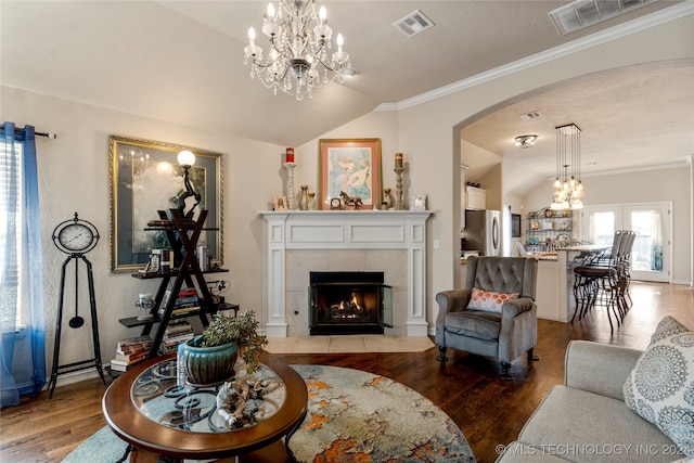 living room with a notable chandelier, vaulted ceiling, hardwood / wood-style flooring, a fireplace, and ornamental molding