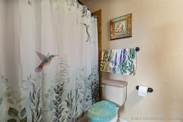 bathroom featuring a shower with shower curtain, a textured wall, and toilet