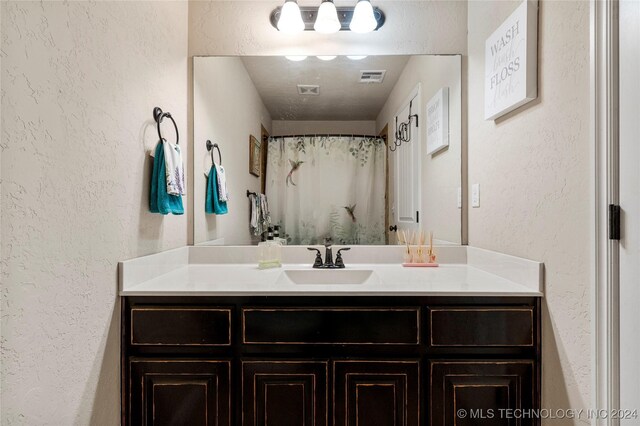 bathroom with visible vents, a textured wall, curtained shower, and vanity